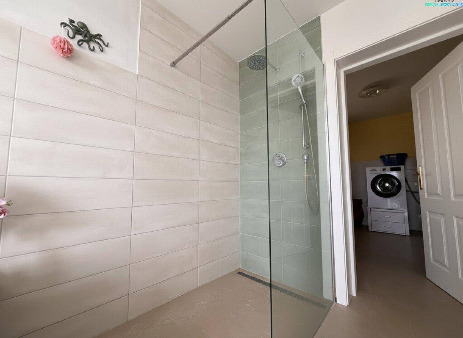 Modernes Badezimmer mit ebenerdiger Dusche und angrenzendem Hauswirtschaftsraum mit Waschmaschine.