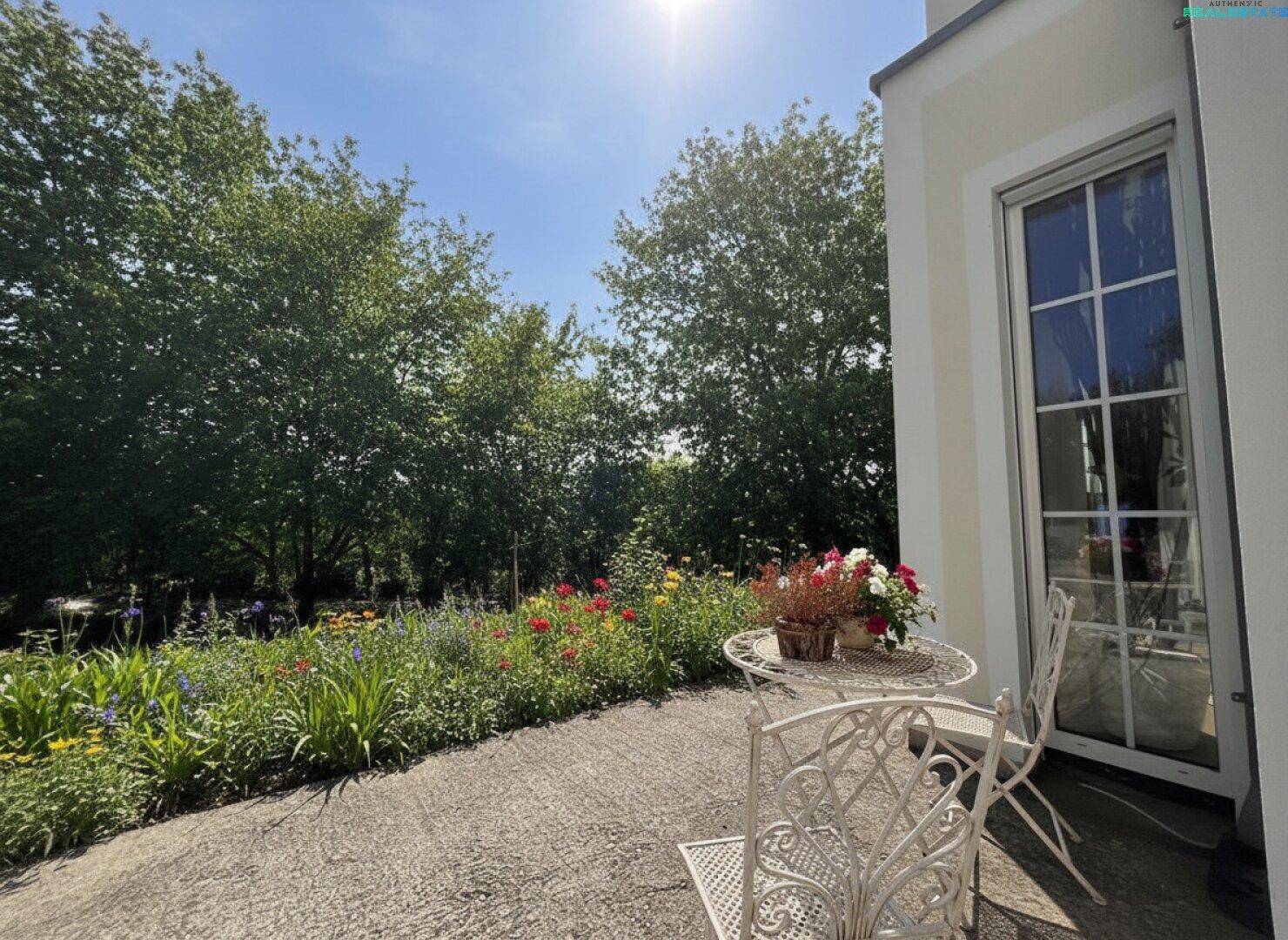 Kleine Terrasse mit Blumenbeeten und Gartenmöbeln in sonniger Lage mit viel Grün.