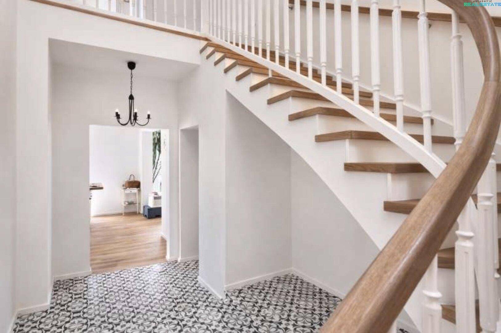 Eleganter Eingangsbereich mit geschwungener Holztreppe und gemustertem Fliesenboden.