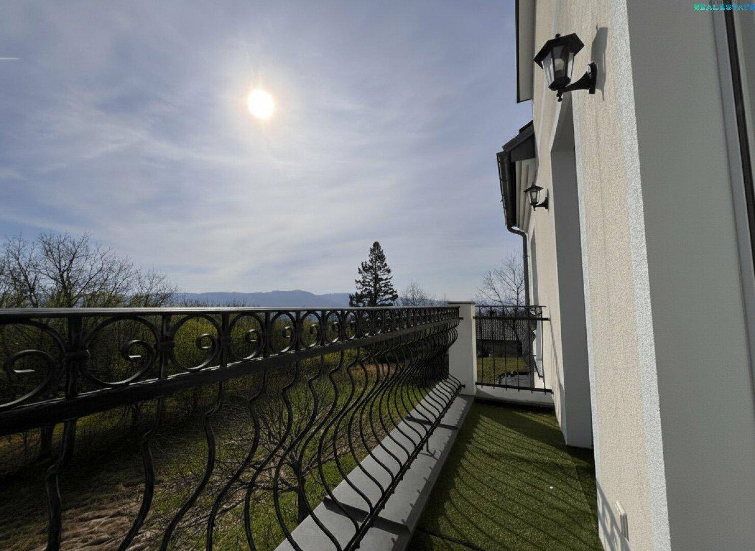 Sonniger Balkon mit schmiedeeisernem Geländer und weitem Blick in die malerische Landschaft.