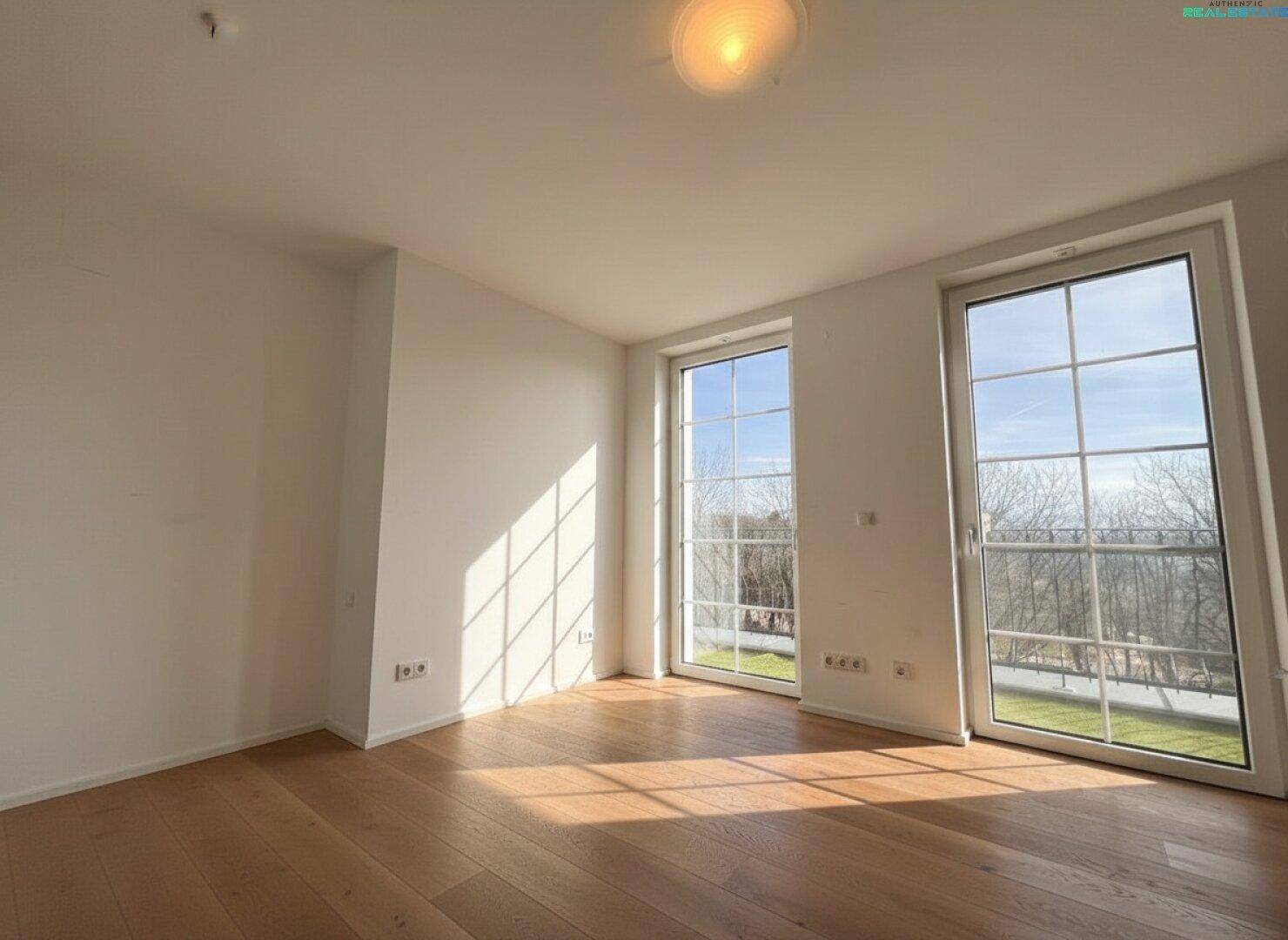 Helles Zimmer mit Holzboden und großen Fenstern, die viel Tageslicht hereinlassen.