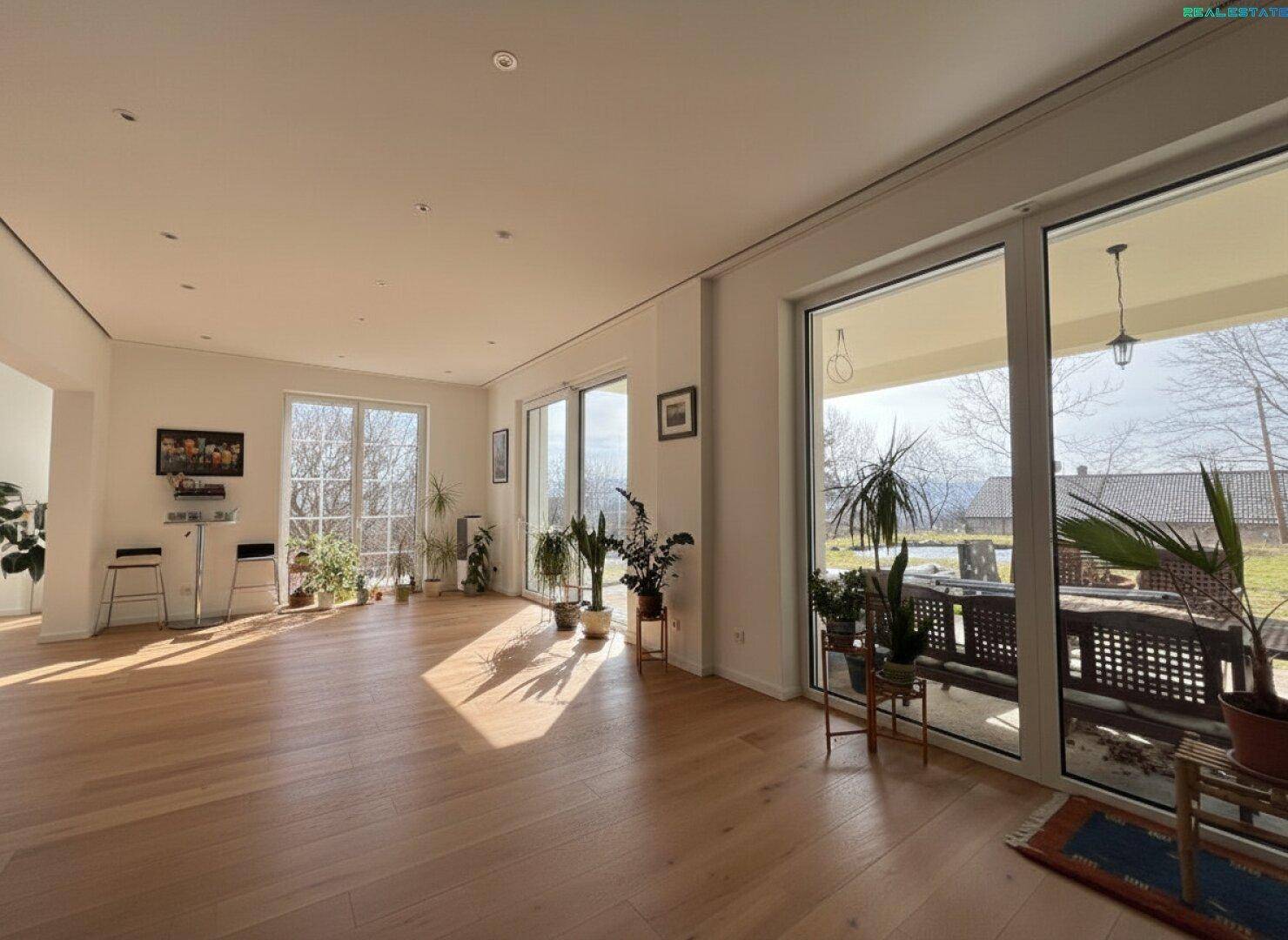 Großzügiger, heller Wohnbereich mit Holzboden und Zugang zur überdachten Terrasse.