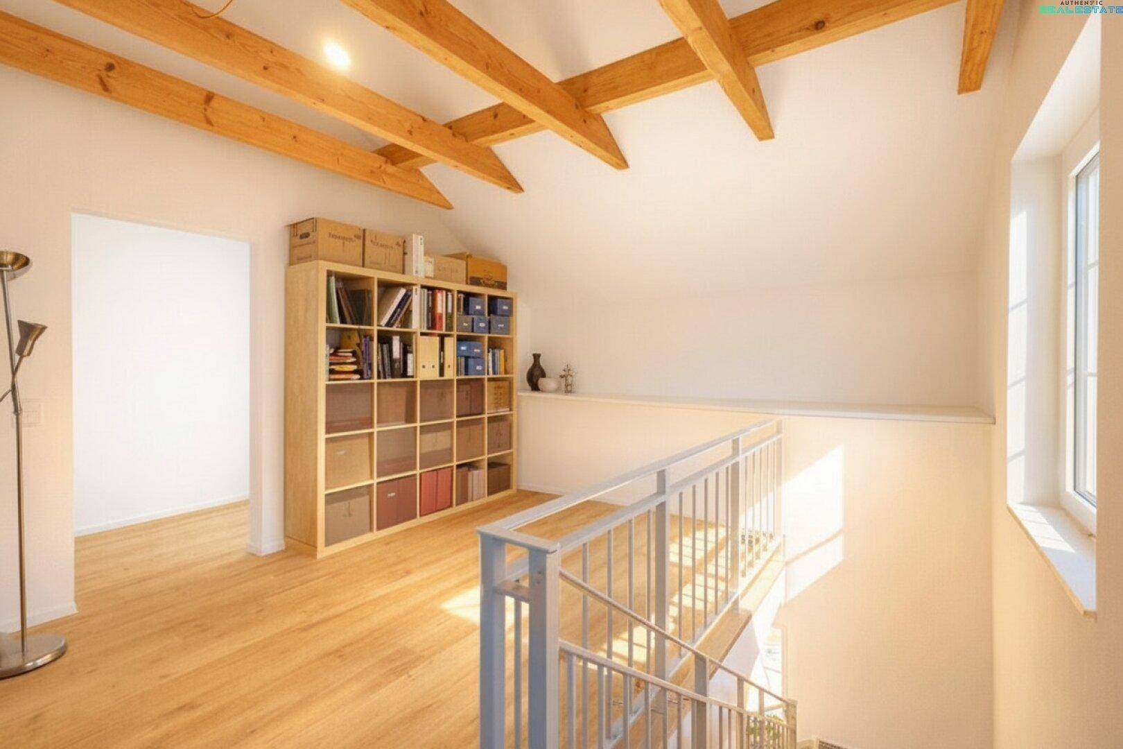 Heller Dachbodenbereich mit Holzbalken, Bücherregal und Treppenaufgang, gut beleuchtet.
