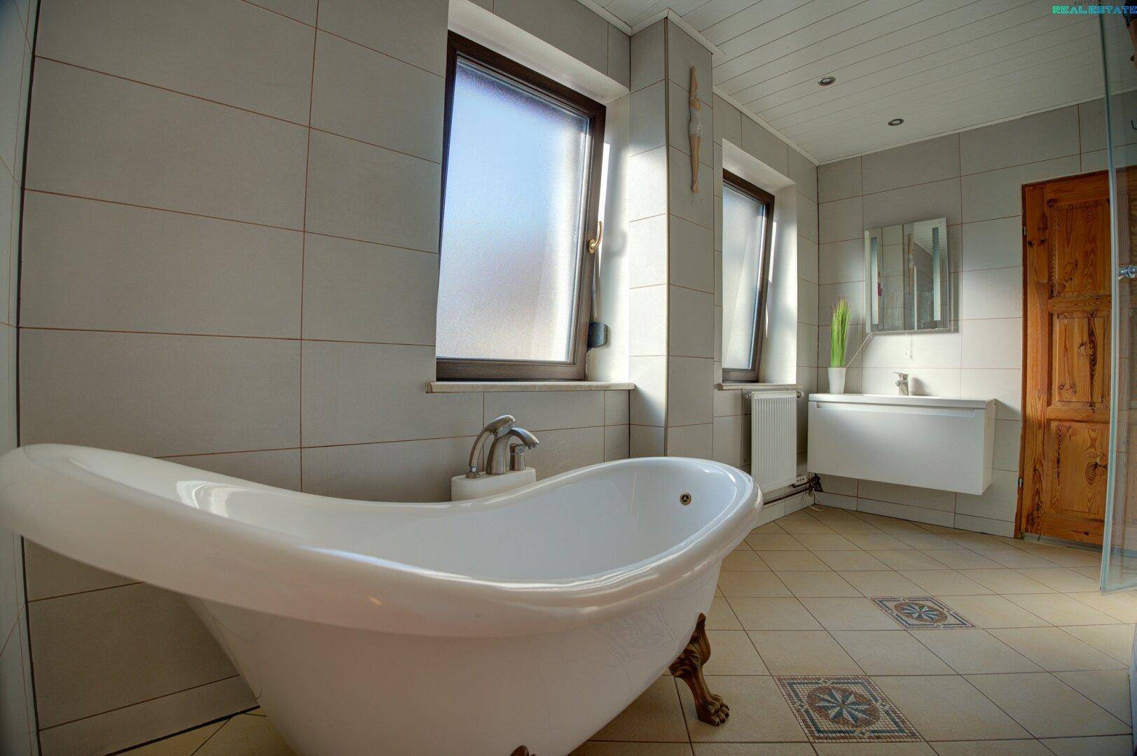 Badezimmer mit freistehender Badewanne, Fliesenboden und Fenster.