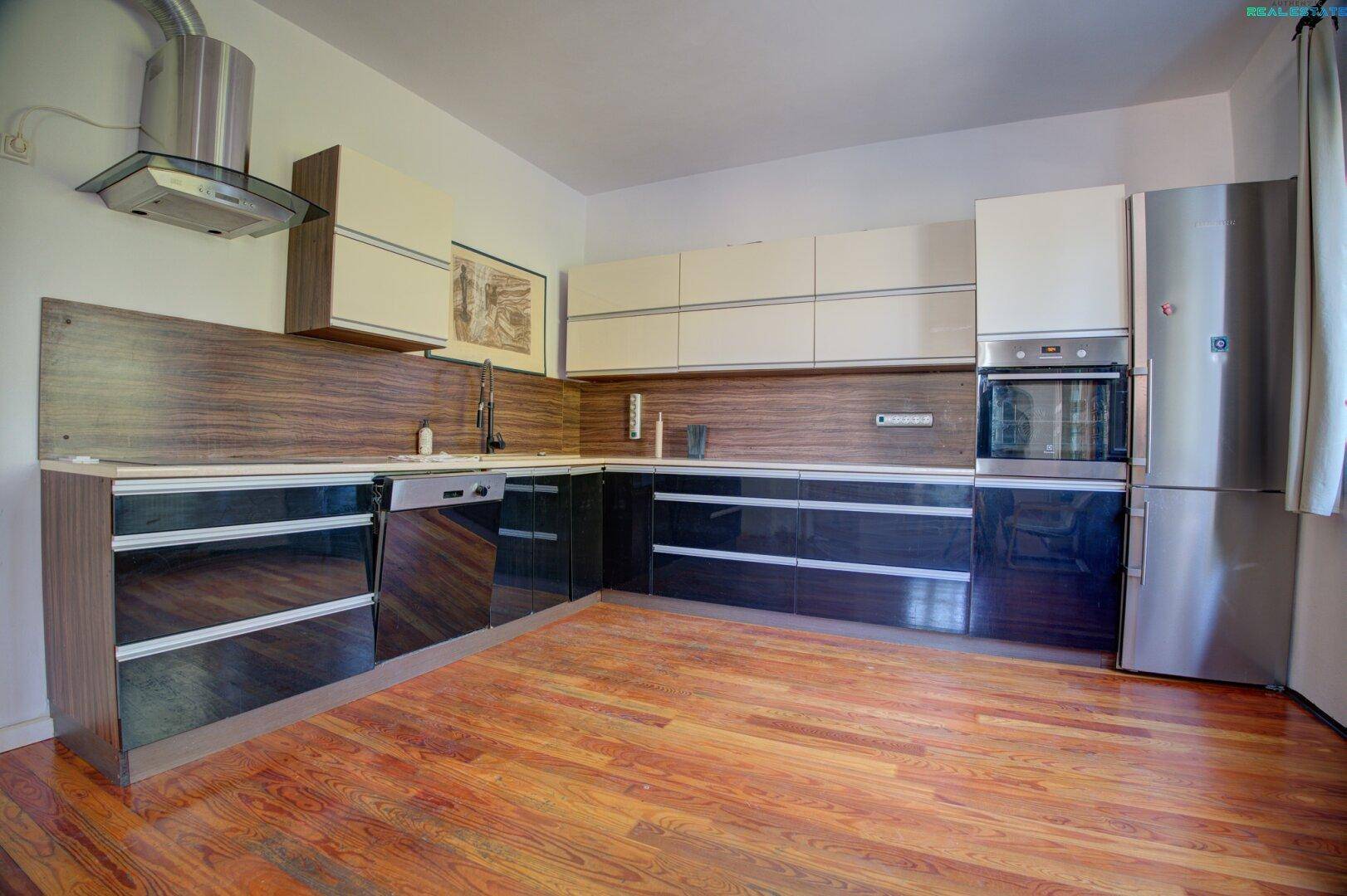 Moderne Küche mit schwarzen Hochglanzfronten, Holzboden und Geräten.