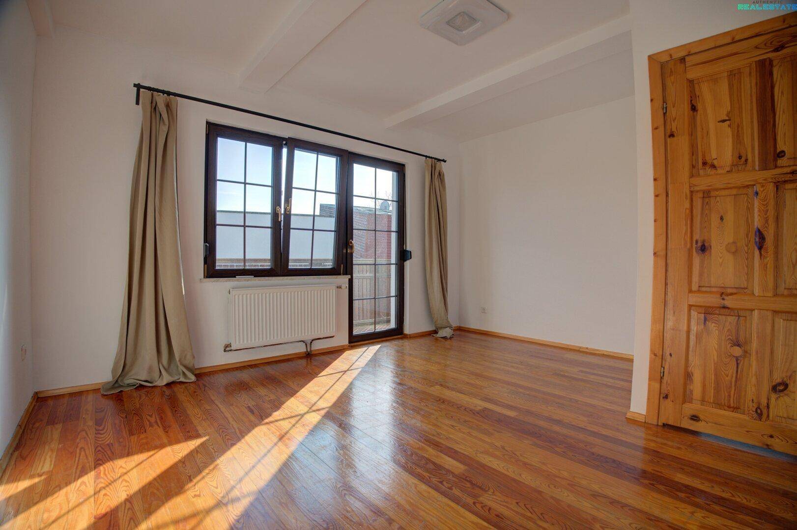 Helles Zimmer mit Holzboden und Zugang zum Balkon.