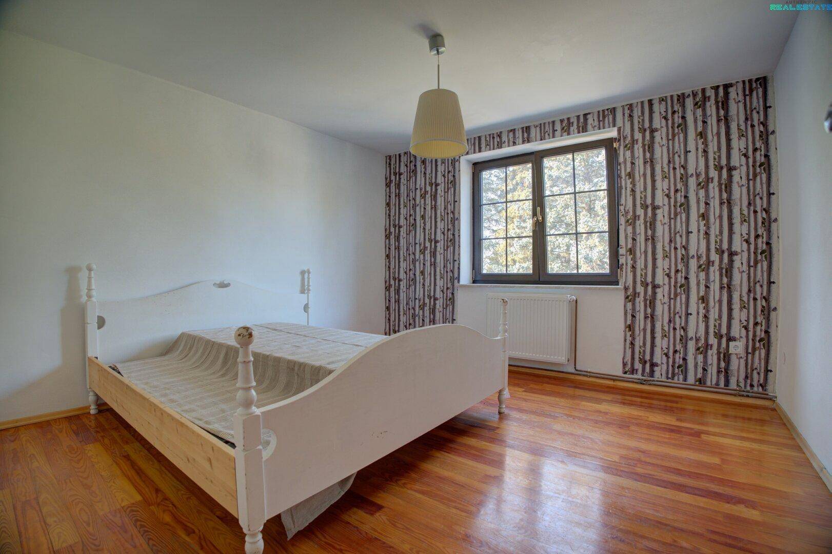 Schlafzimmer mit Holzboden, Doppelbett und Fensterblick ins Grüne.