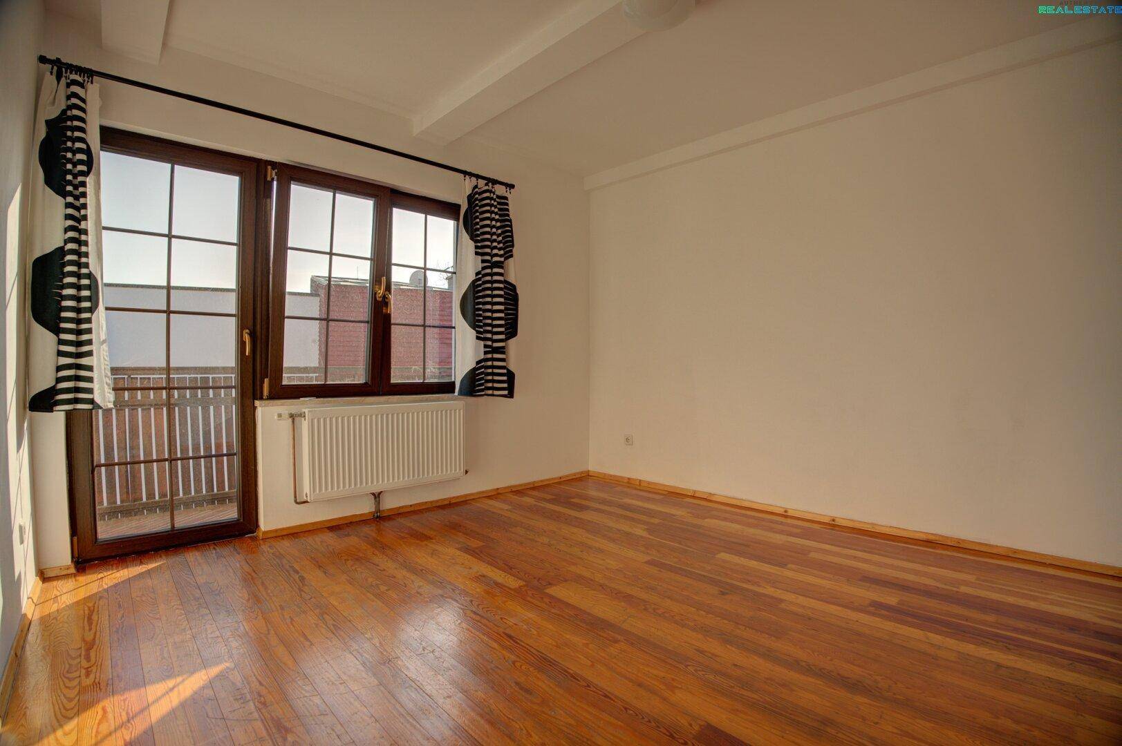 Helles Zimmer mit Holzboden und Zugang zum Balkon.