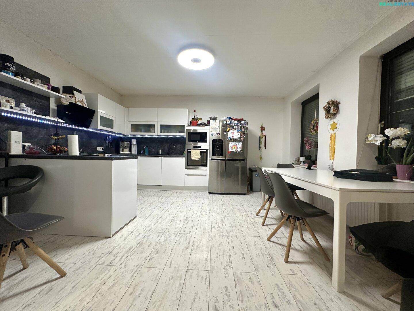 Moderne weiße Küche mit integrierten Geräten, Essbereich und Fliesenboden.