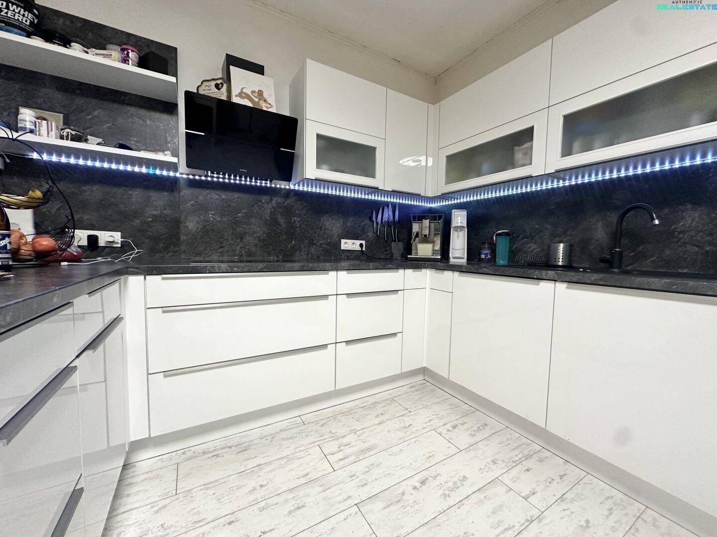 Detailansicht der modernen weißen Küche mit dunkler Arbeitsplatte und LED-Beleuchtung.