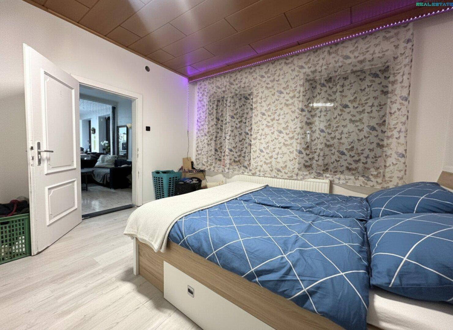 Schlafzimmer mit Doppelbett, Holzdecke und Blick in den Wohnbereich.