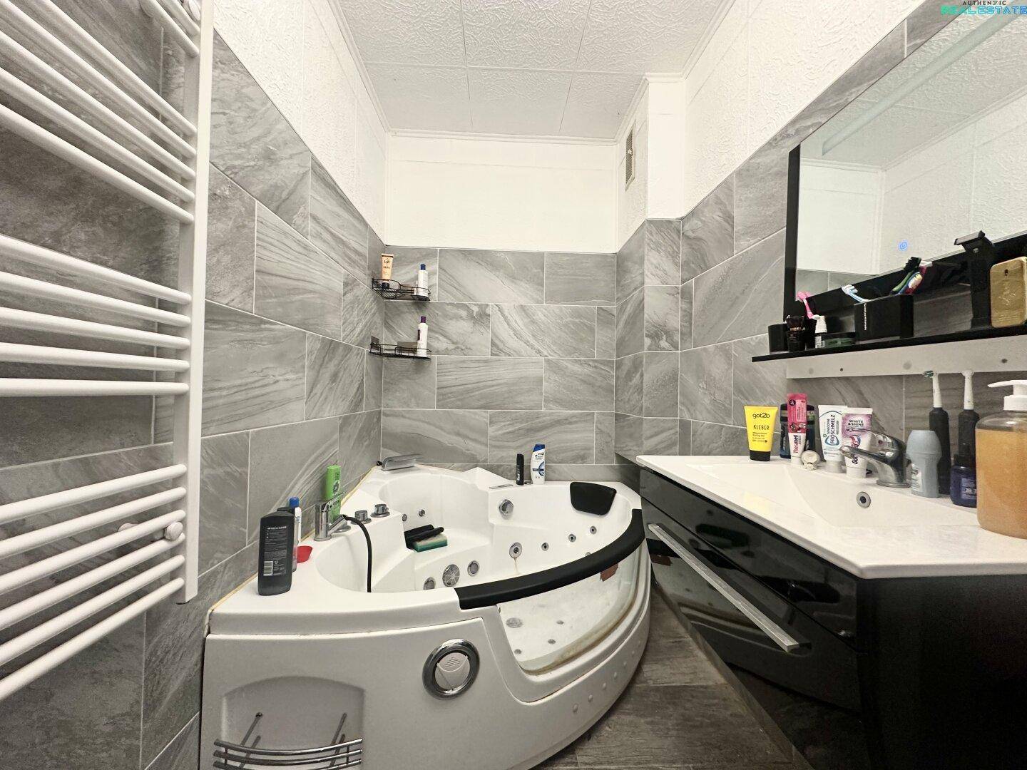Modernes Badezimmer mit Whirlpool-Badewanne, grauen Fliesen und beheiztem Handtuchhalter.