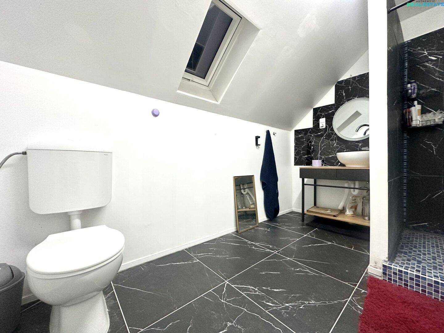 Toilette im modernen Dachgeschoss-Badezimmer mit schwarzem Fliesenboden und Dachfenster.