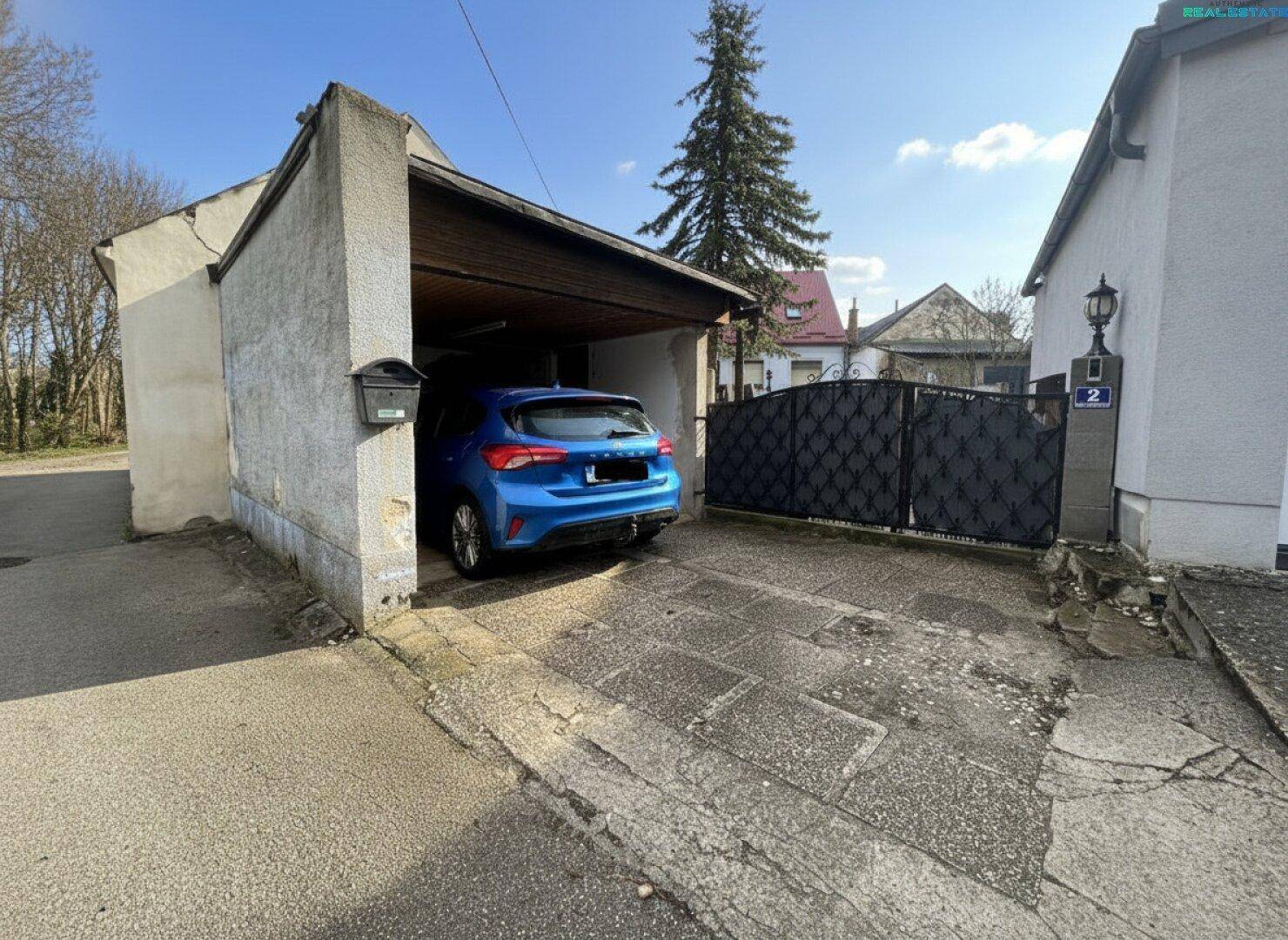 Überdachter Stellplatz oder Carport mit Einfahrt und Metalltor.