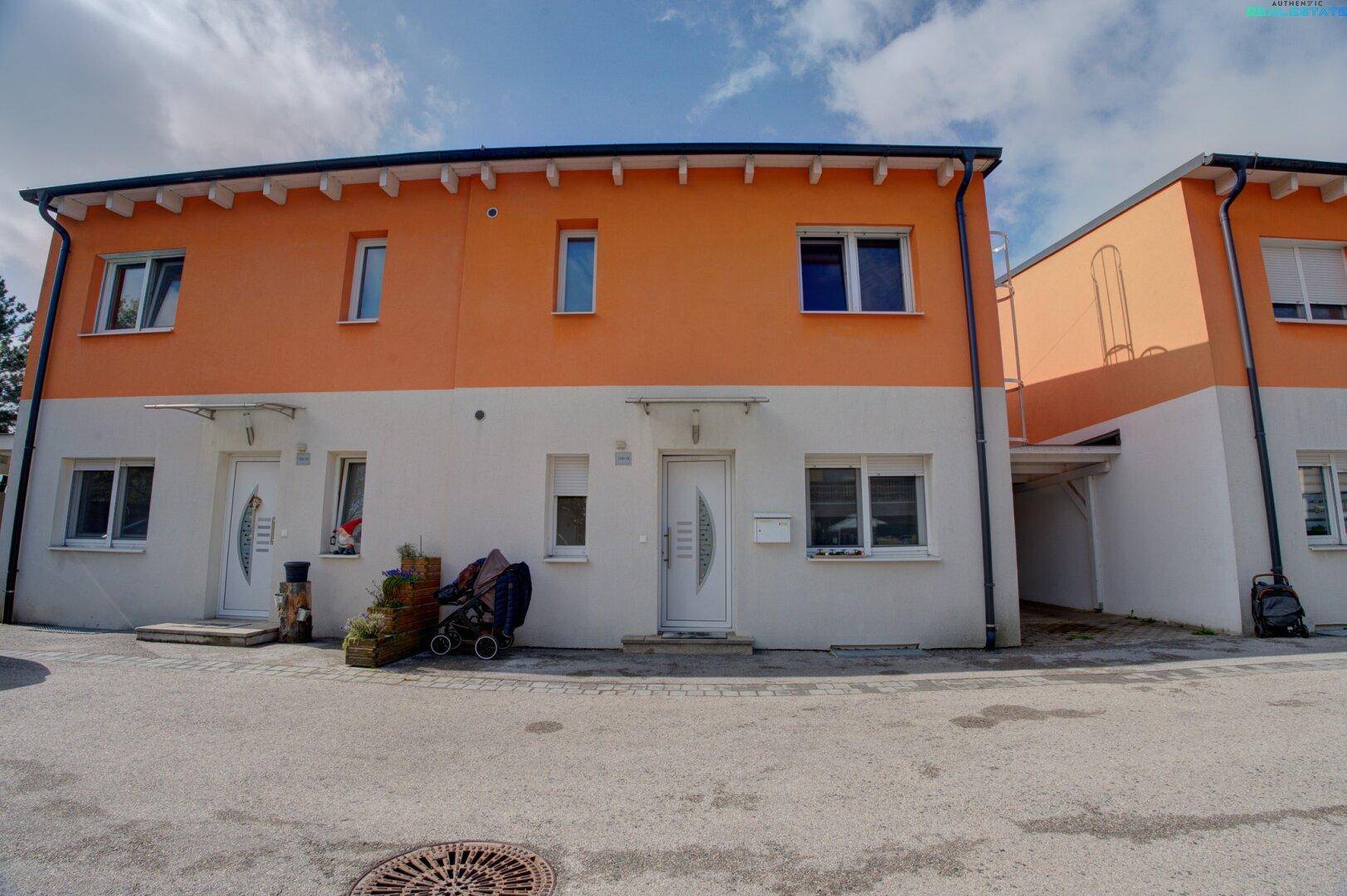 Vorderansicht der modernen Reihenhäuser mit leuchtend orangefarbener und weißer Fassade.