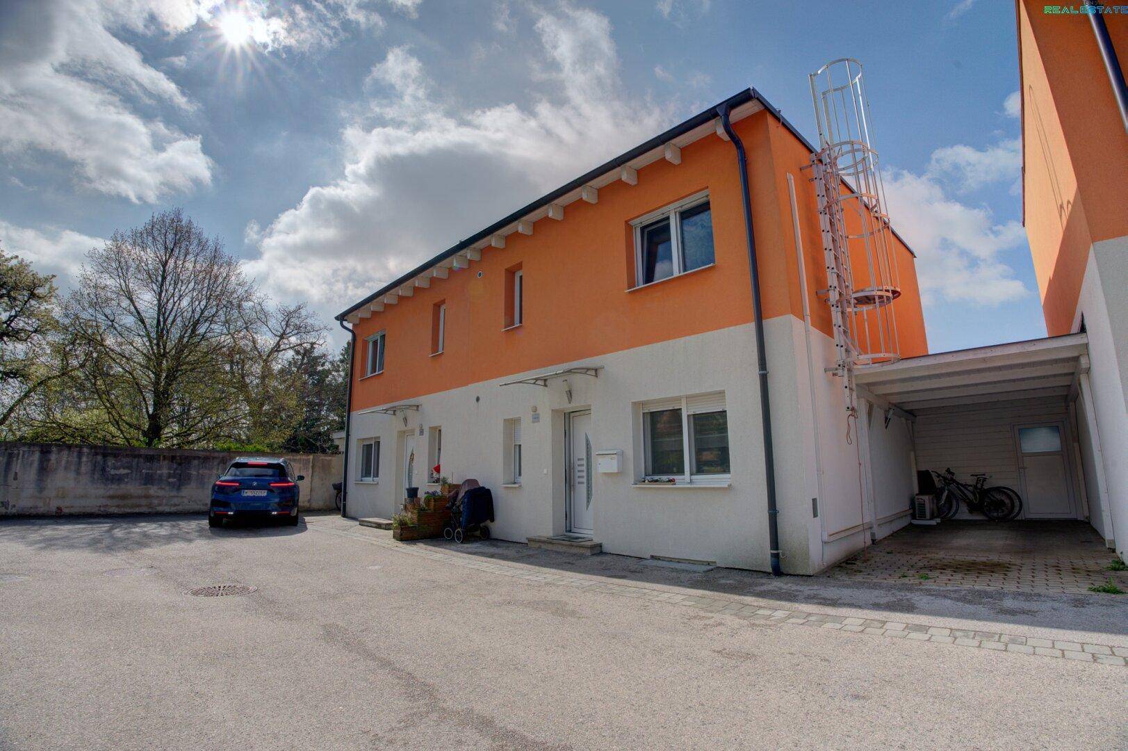 Reihenhaus mit Carport und zusätzlichem Parkplatz im Freien vor der Fassade.