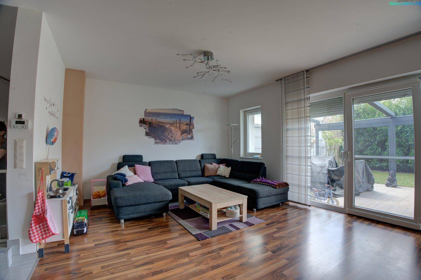 Gemütliches Wohnzimmer mit dunklem Holzboden und direktem Zugang zur Terrasse und zum Garten.