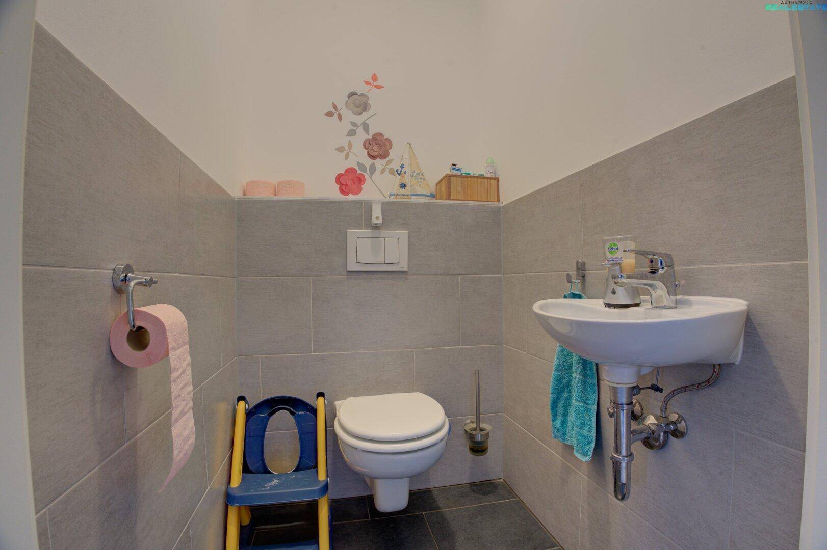 Modern gefliestes Gäste-WC mit Wand-WC, kleinem Waschbecken und dekorativer Wandgestaltung.