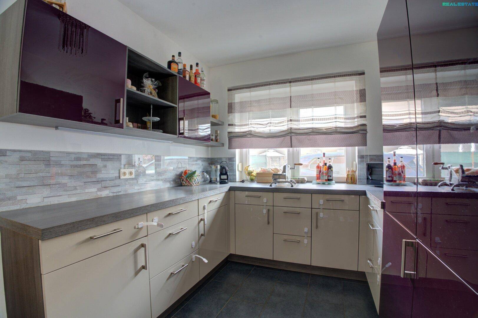 Helle Küche mit Fenster, beigen Unterschränken und glänzenden violetten Oberschränken.