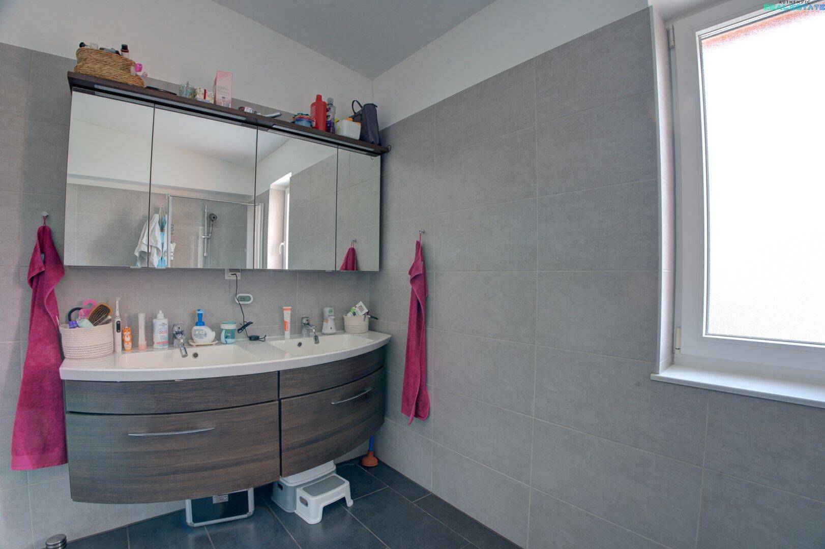 Badezimmer mit Doppelwaschbecken, großem Spiegelschrank und einem Fenster.