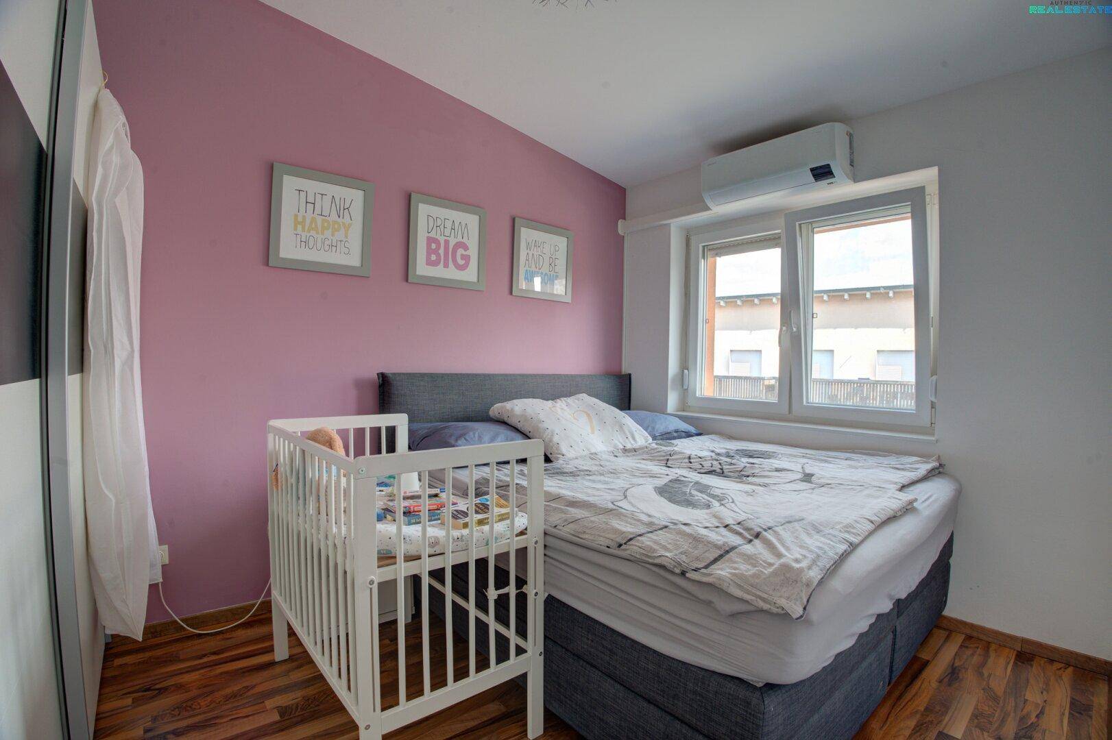 Schlafzimmer mit Doppelbett, Kinderbett und installierter Klimaanlage an der Wand.