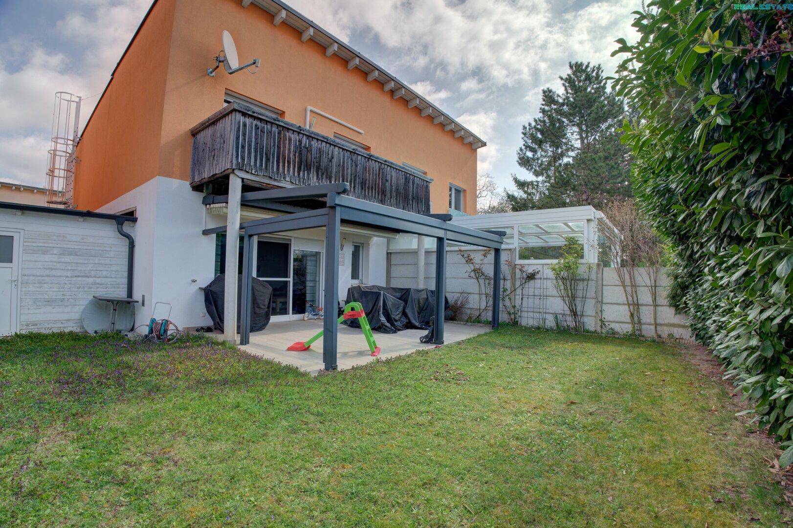 Gepflegter Garten mit Rasenfläche und einer überdachten Terrasse am Haus.