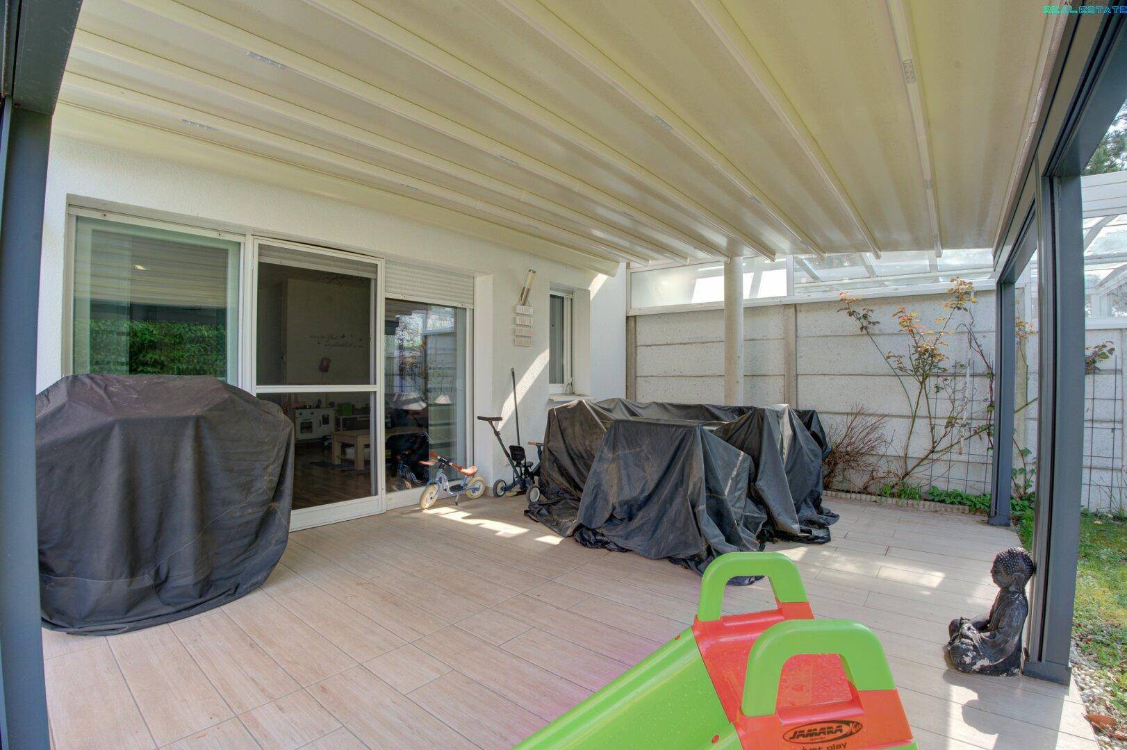 Großzügige überdachte Terrasse mit Fliesenboden, ideal für Gartenmöbel und Entspannung.