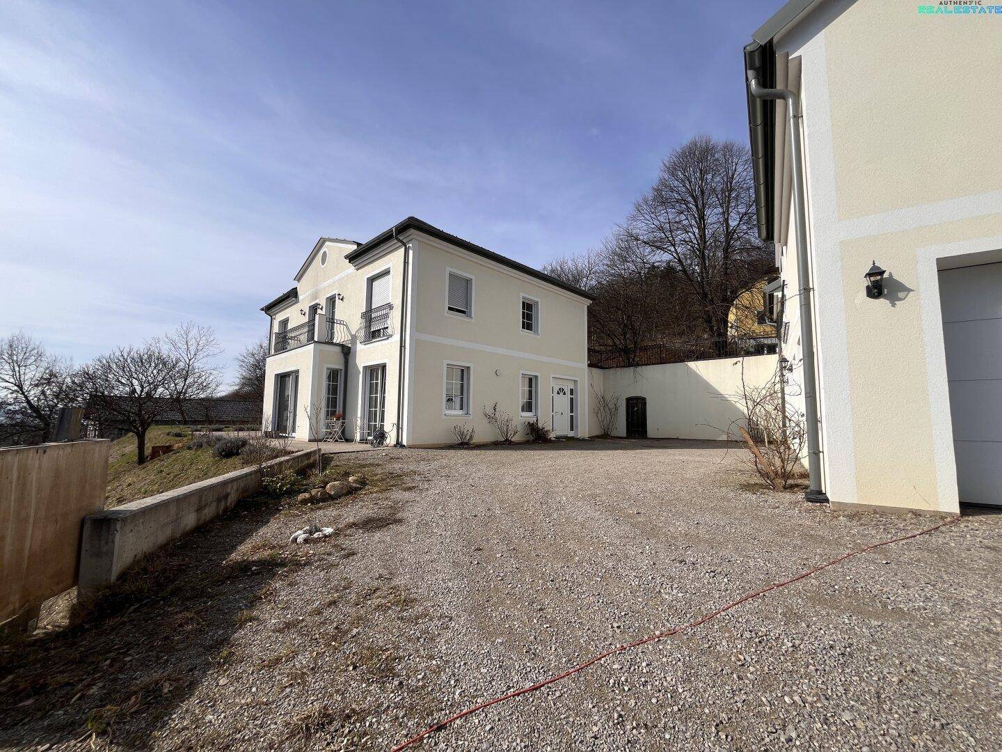 Vorderansicht des Hauses mit Kiesauffahrt und angrenzendem Garagengebäude.