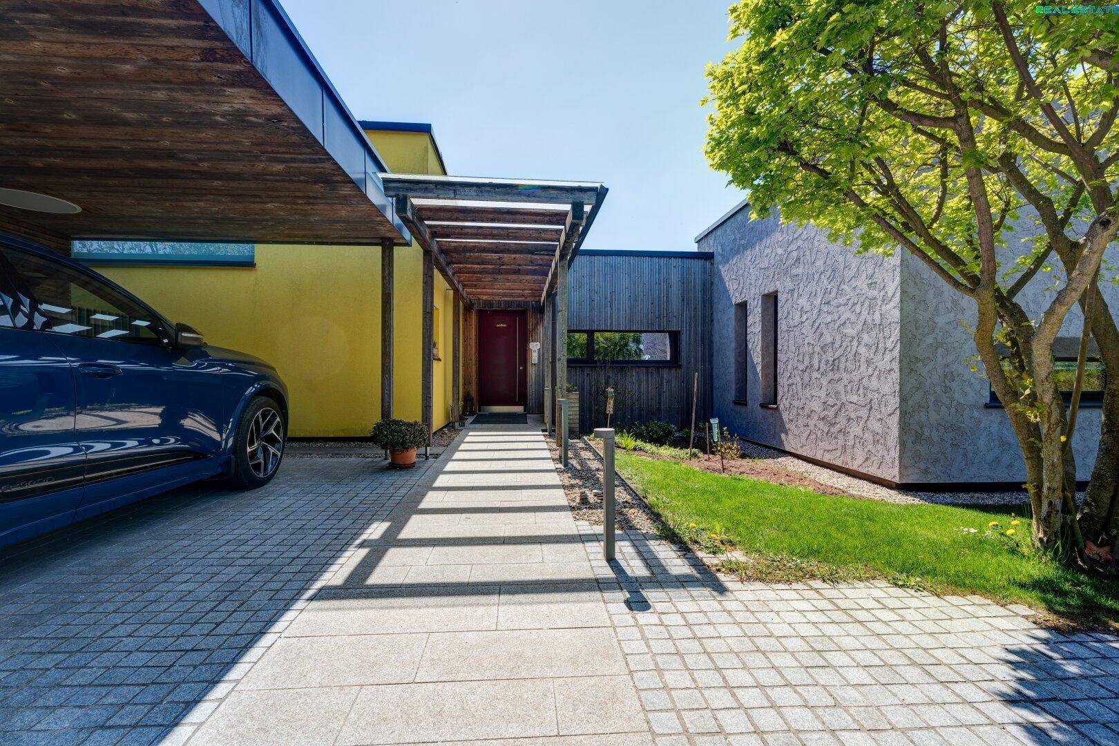 Moderner Eingangsbereich mit Carport, gepflastertem Zugang und Holzelementen an der Fassade.
