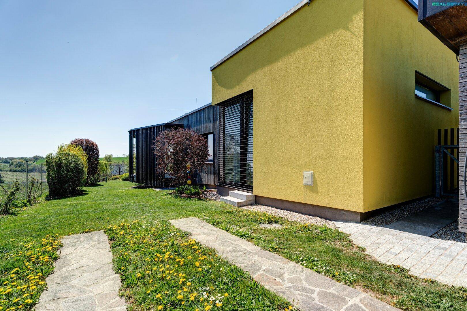 Seitlicher Blick auf das Haus mit gelber Fassade, Rasenfläche und Steinpfaden im Garten.