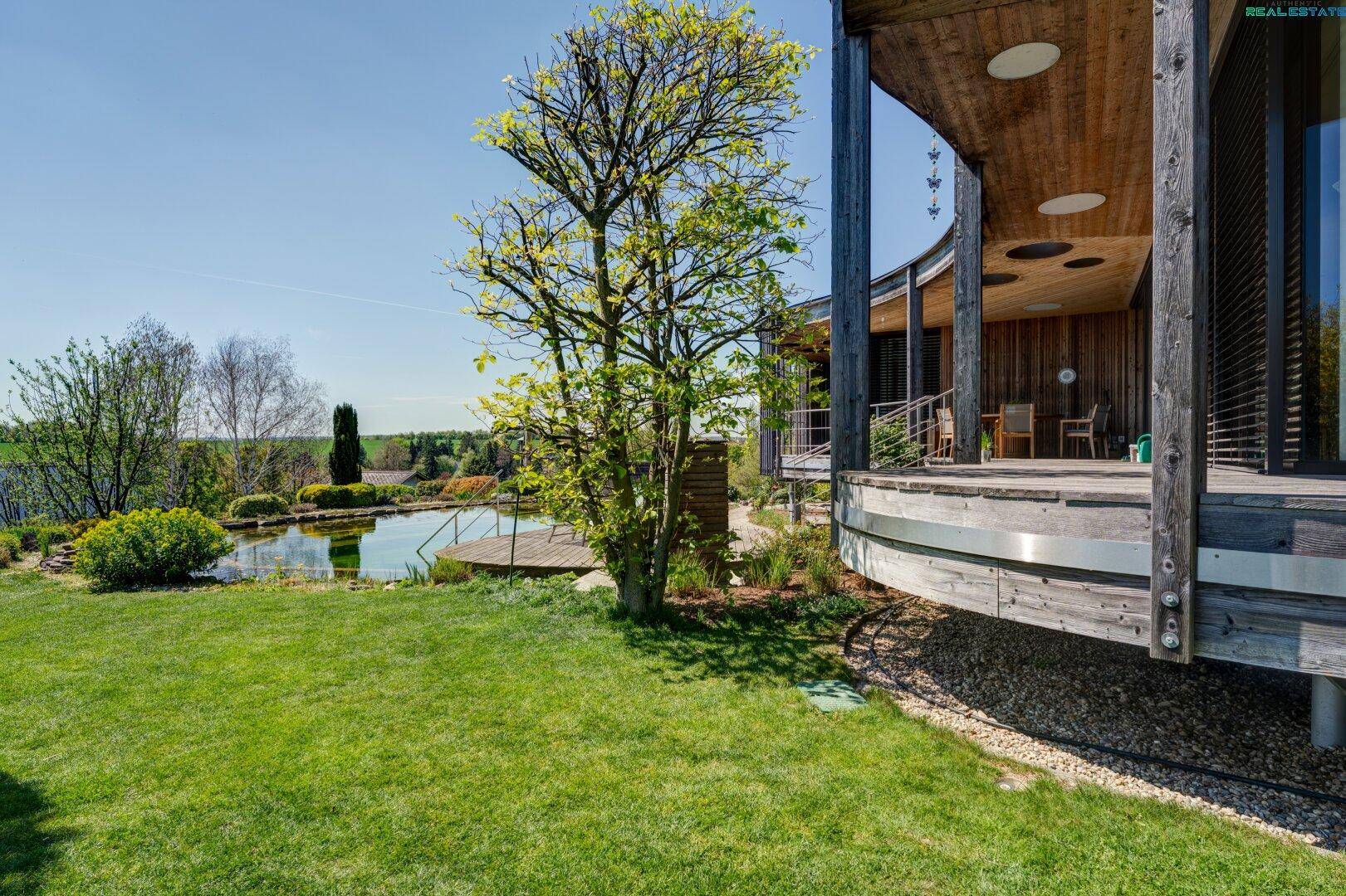 Gartenansicht mit Naturpool, Holzdeck und der geschwungenen Holzfassade des modernen Hauses.