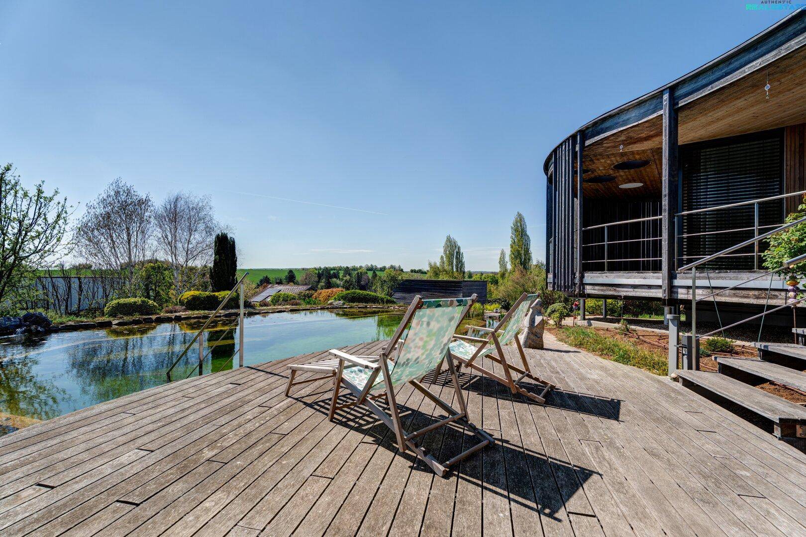 Geräumiges Holzdeck mit Liegestühlen am Naturpool, ideal zum Entspannen im Freien.