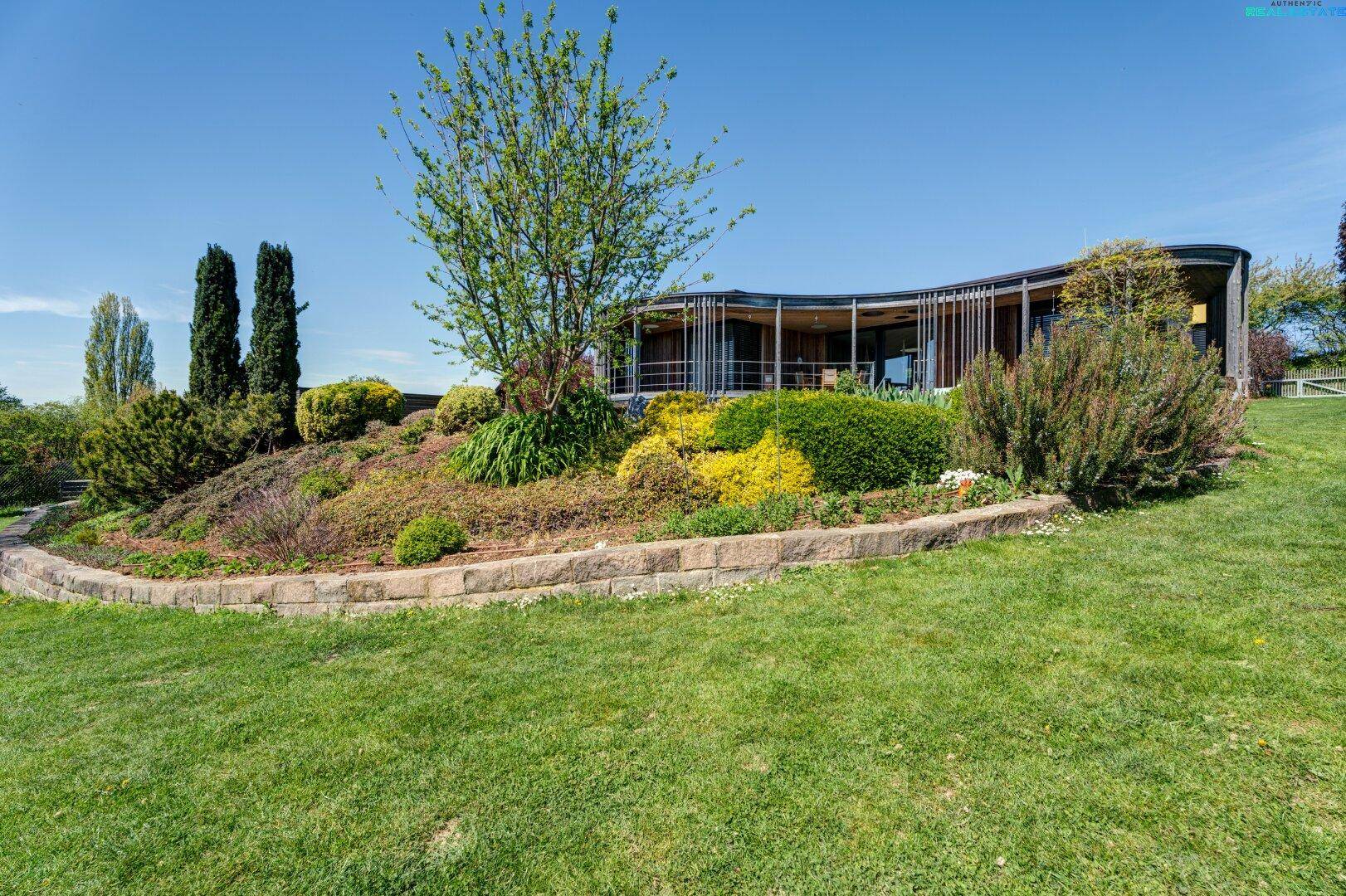 Gepflegter Garten mit Rasenflächen, Blumenbeeten und einer Steinmauer im Vordergrund.