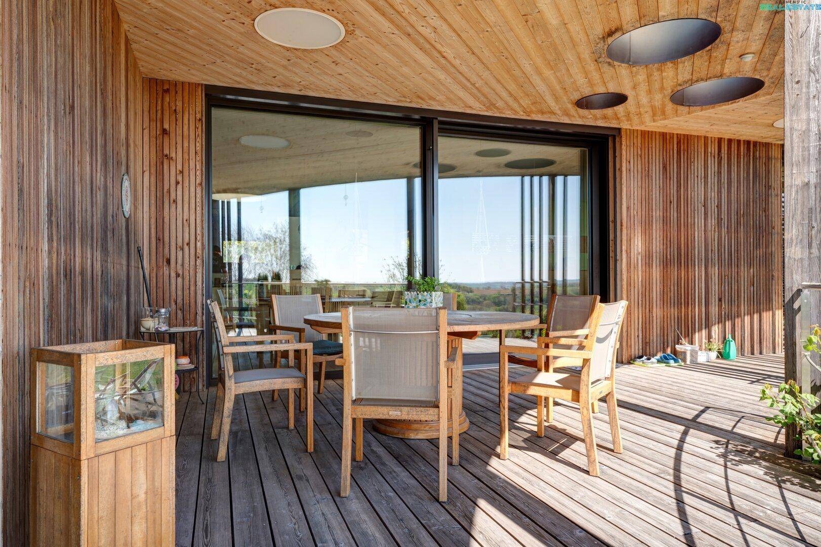 Essbereich auf der überdachten Holzterrasse mit modernen Gartenmöbeln und Schiebetüren zum Innenraum.