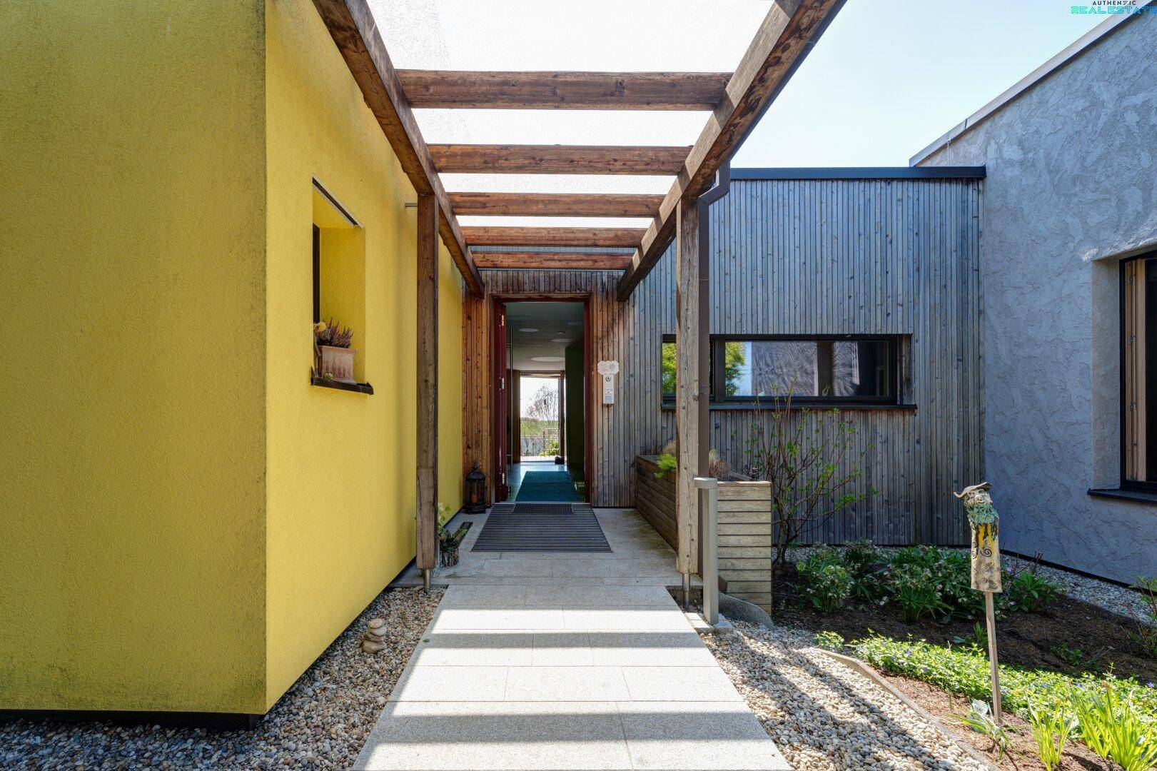 Überdachter Eingangsbereich mit Holzpergola und gepflastertem Weg zum Haus.
