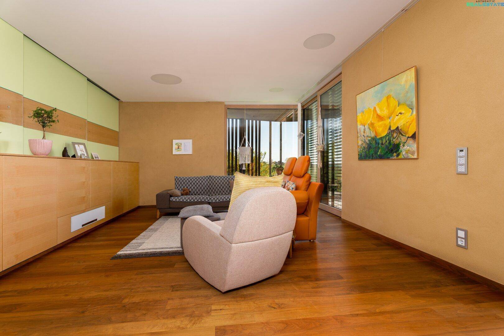 Modernes Wohnzimmer mit Holzboden, bequemen Möbeln und großen Fenstern mit Blick ins Grüne.