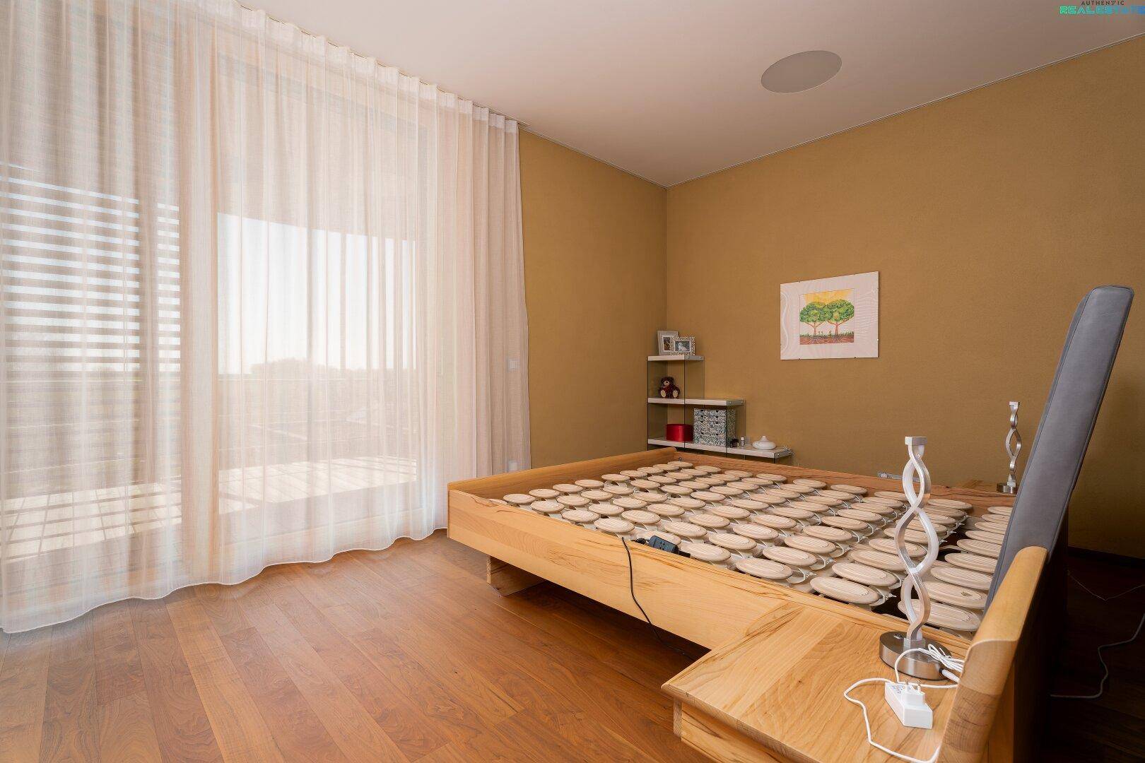 Helles Schlafzimmer mit Holzboden und großen Fenstern, die viel Tageslicht hereinlassen.