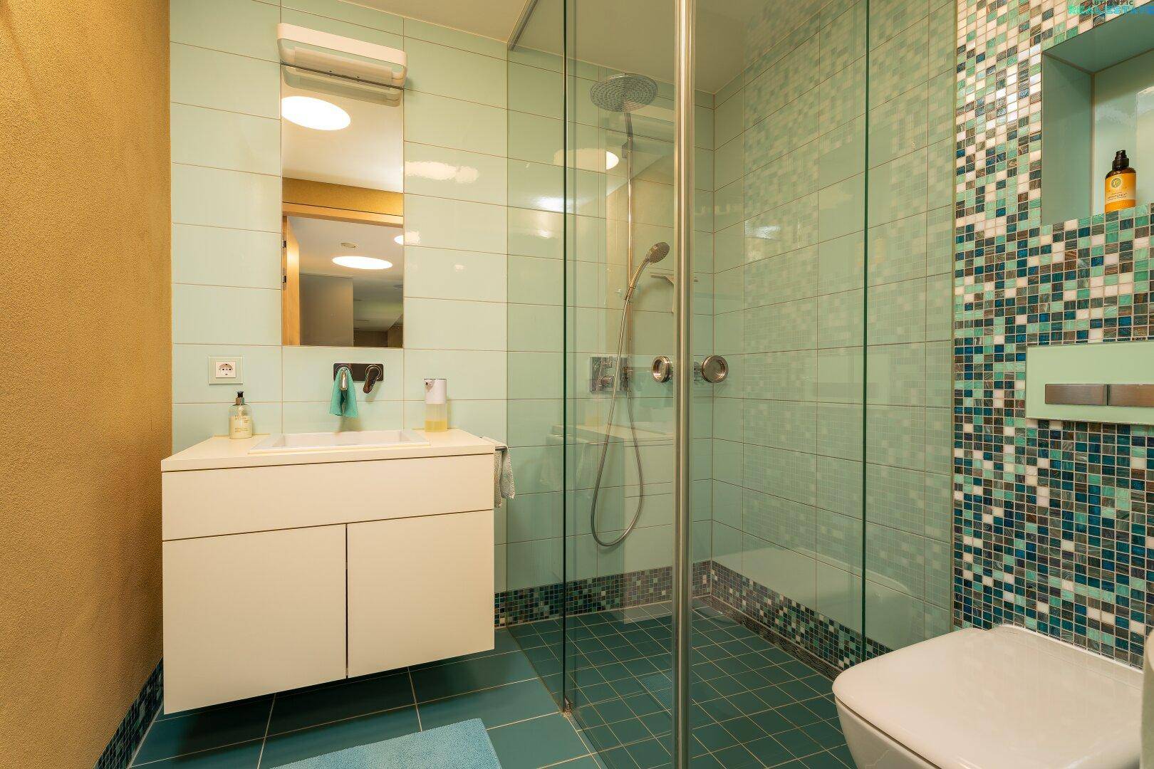 Modernes Badezimmer mit Duschkabine, Einzelwaschbecken und blauen Mosaikfliesen.
