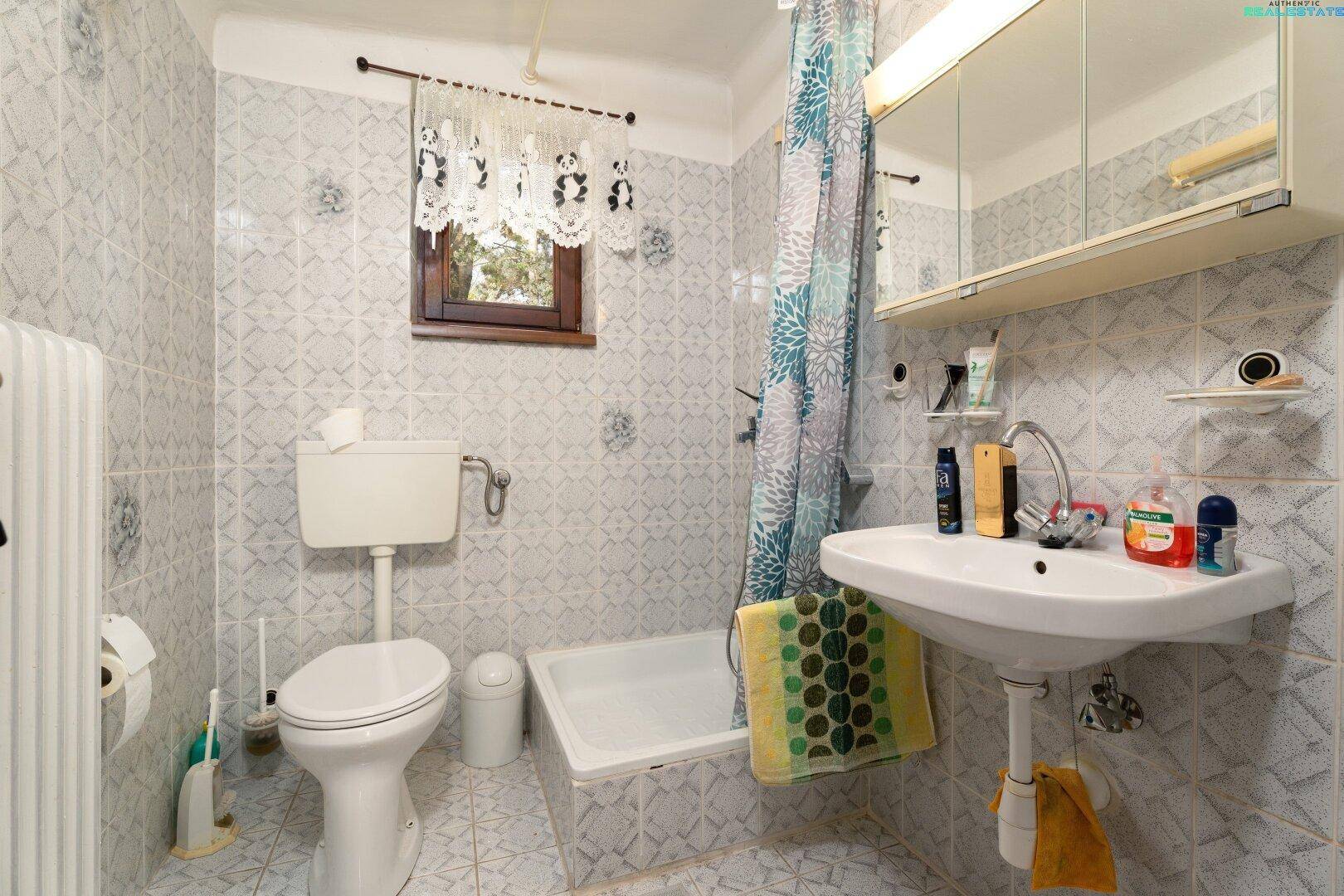 Badezimmer mit hellen Fliesen, Badewanne, WC und Waschbecken, ausgestattet mit Spiegelschrank.