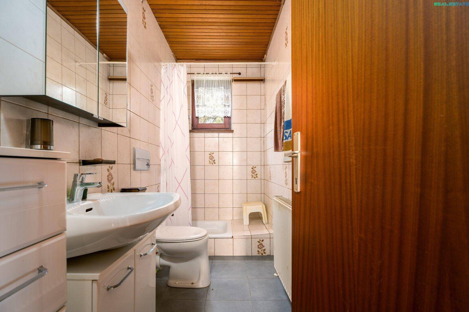 Kleines Badezimmer mit Dusche, WC und Waschbecken, Holzwänden und einem Fenster.