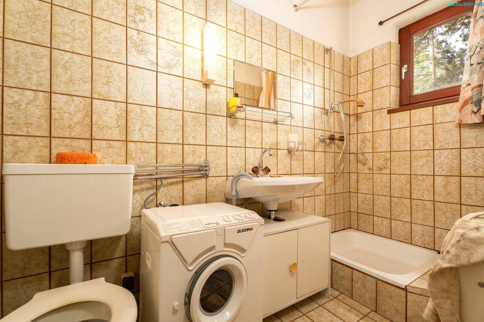 Badezimmer mit beigen Fliesen, Badewanne, WC und Waschmaschine, ideal für den Familiengebrauch.