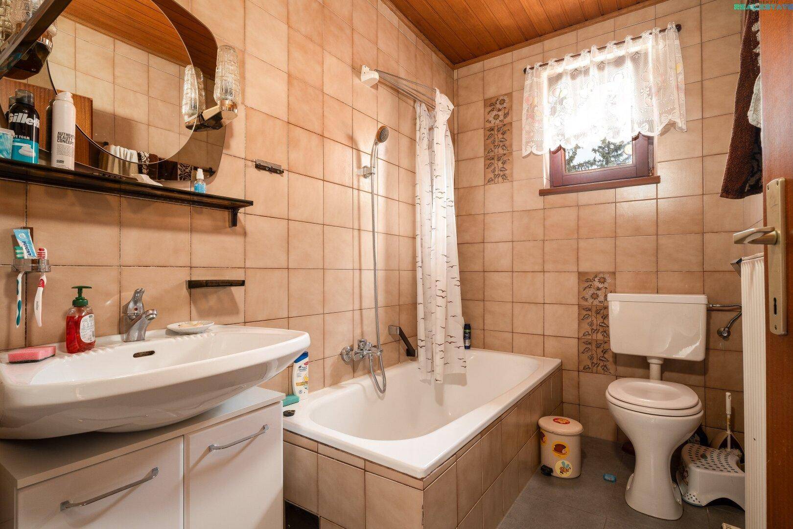 Geräumiges Badezimmer mit Badewanne, WC und Waschbecken, umgeben von warmen Fliesen.