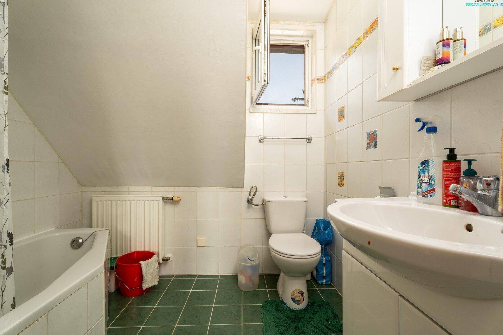 Badezimmer im Dachgeschoss mit Badewanne, WC und Waschbecken, hell gefliest und mit Fenster.