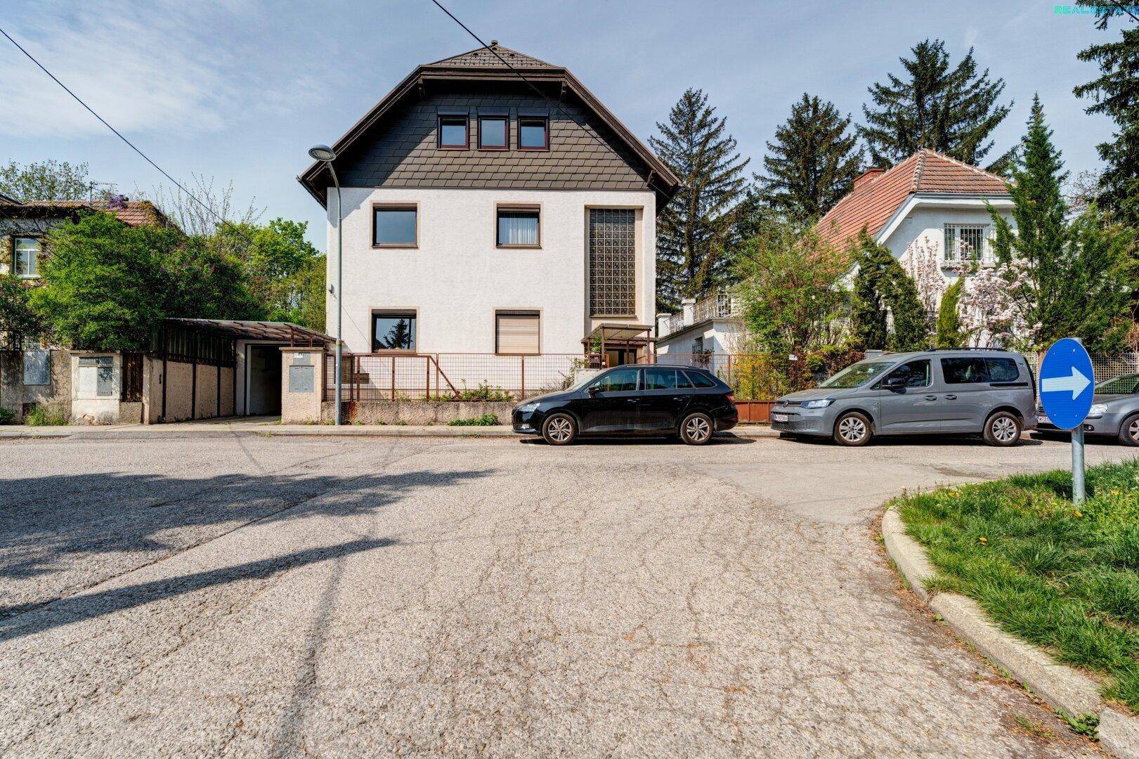 Freistehendes Einfamilienhaus mit weißer Fassade und dunklem Dach, umgeben von Bäumen.