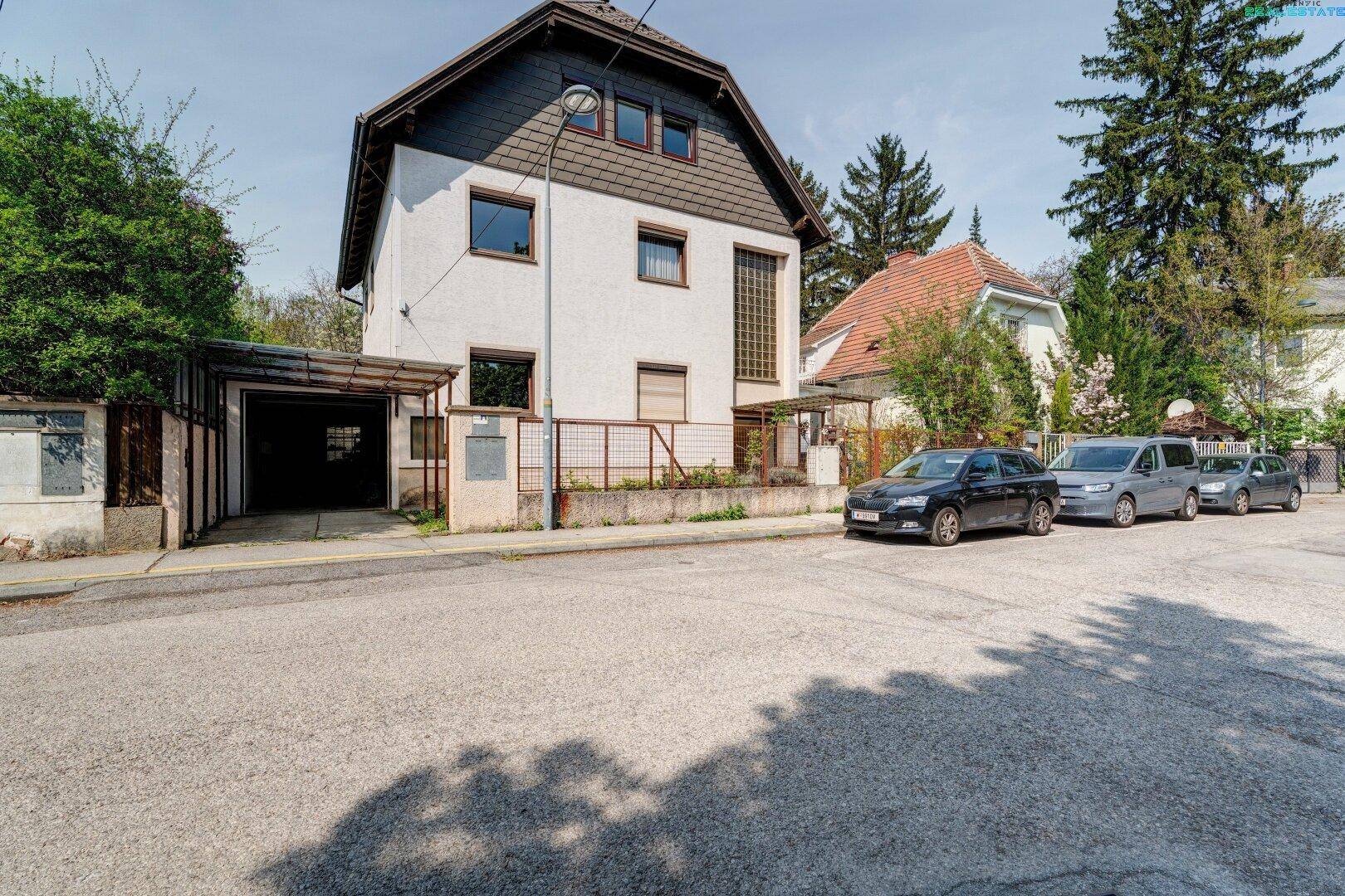 Vorderansicht des Hauses von der Straße aus mit angrenzendem Carport und parkenden Autos.
