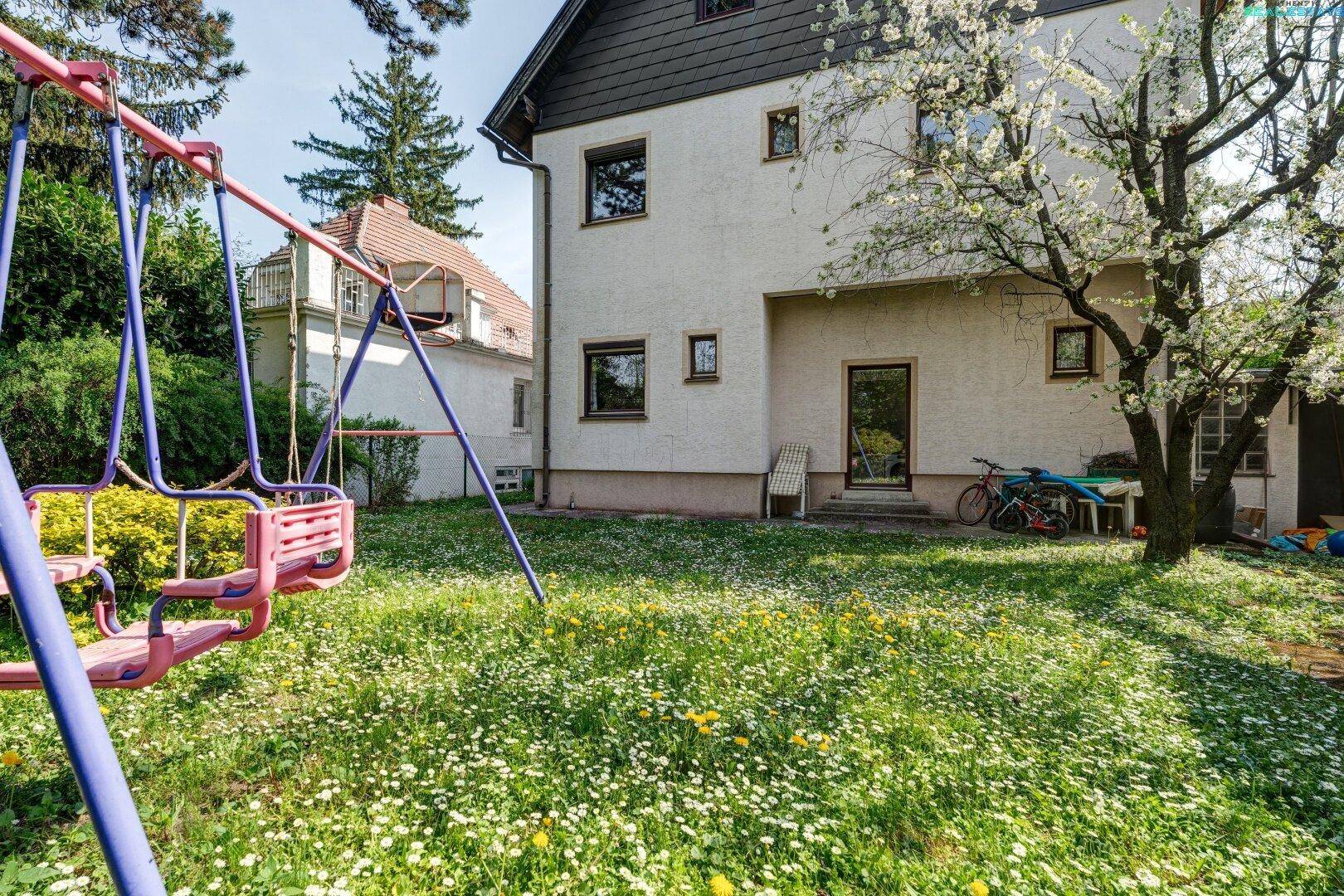 Großer Garten hinter dem Haus mit Schaukel und viel Grünfläche für Kinder zum Spielen.