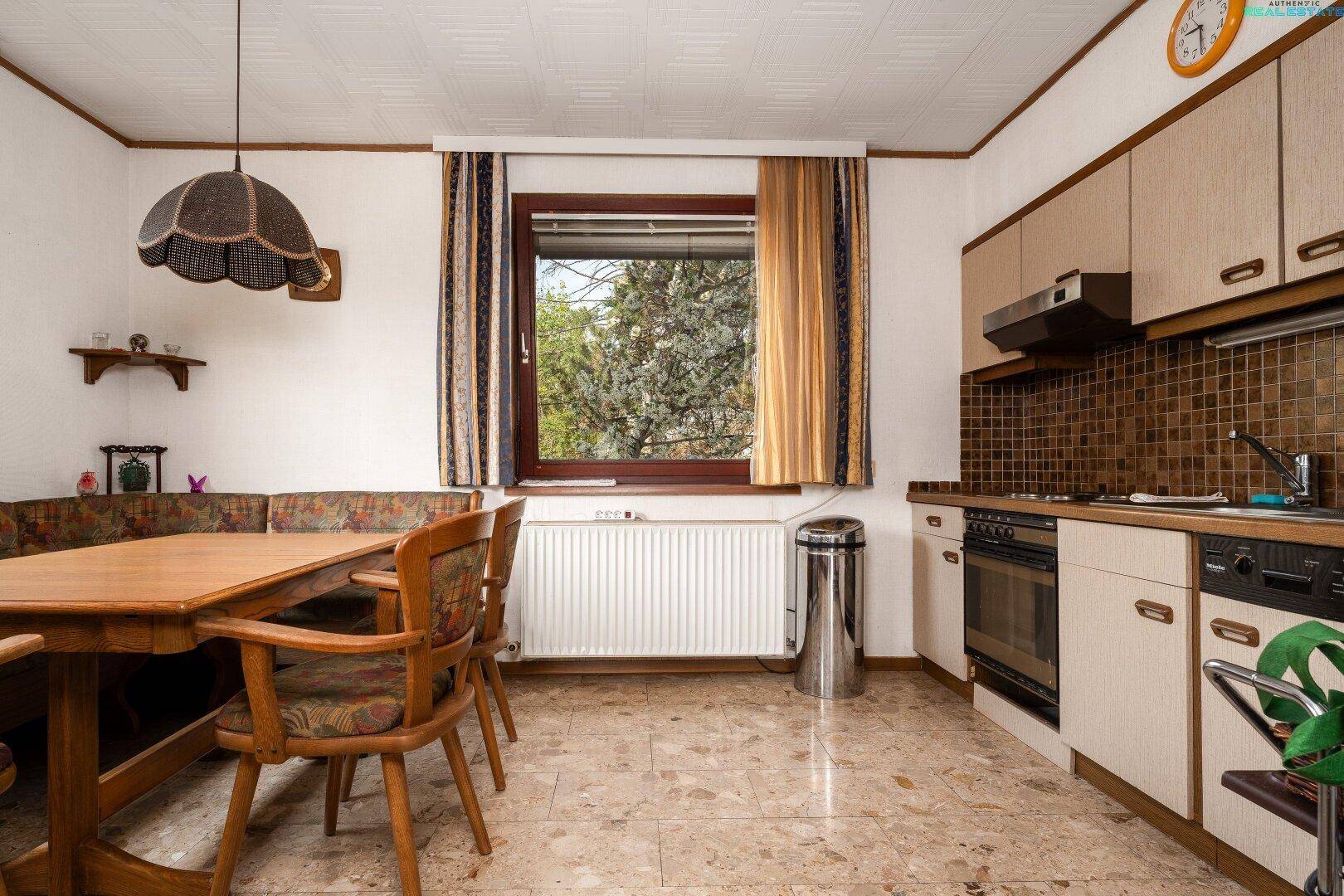 Funktionale Küche mit Essbereich, Einbauschränken und Blick ins Grüne durch das Fenster.