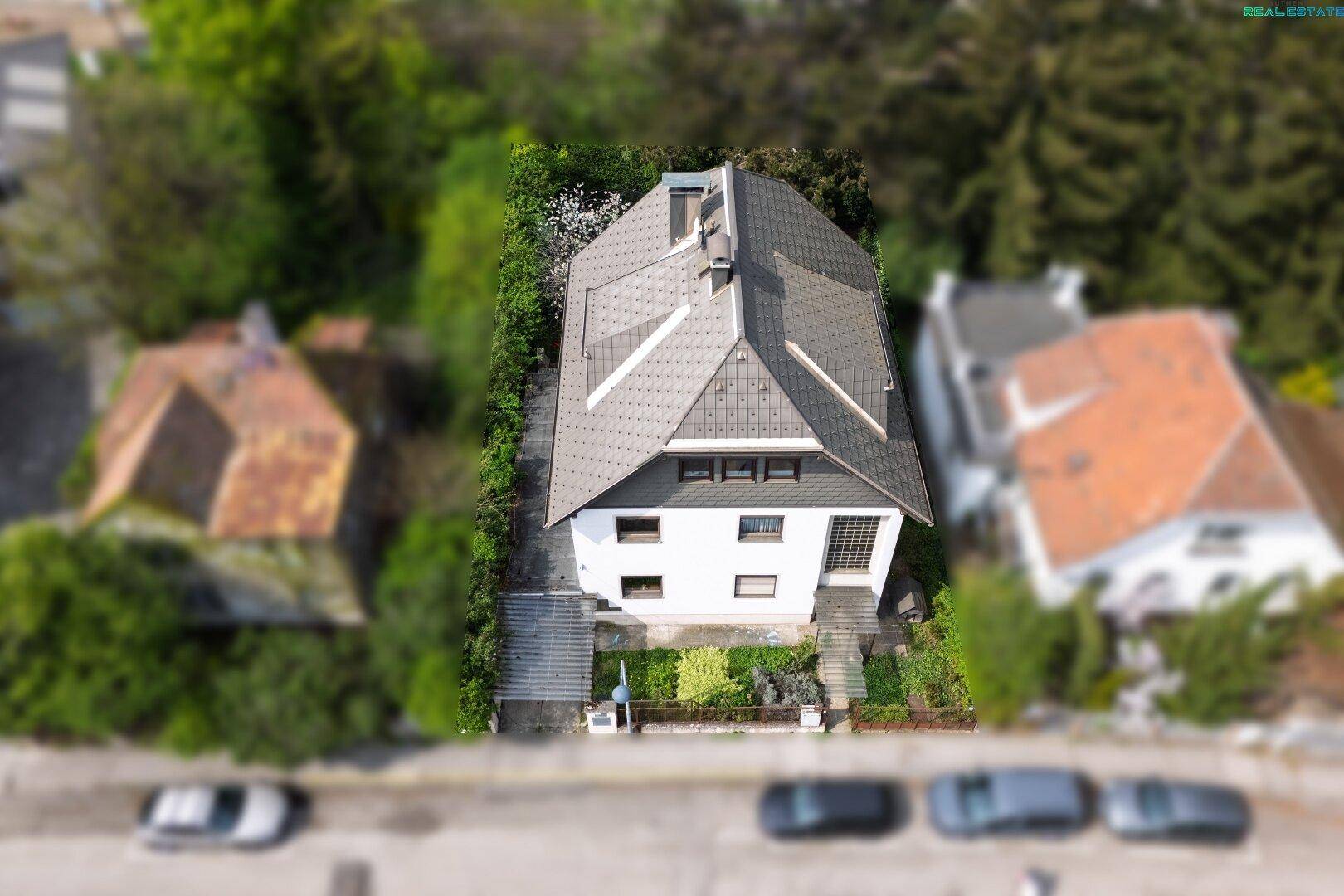 Ansicht von oben auf ein Wohngebäude mit grauem Dach und einem kleinen Vorgarten an der Straße.