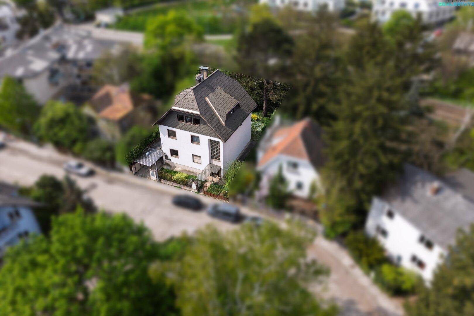 Vogelperspektive eines Wohnhauses mit dunklem Dach und üppiger Vegetation in der Umgebung.