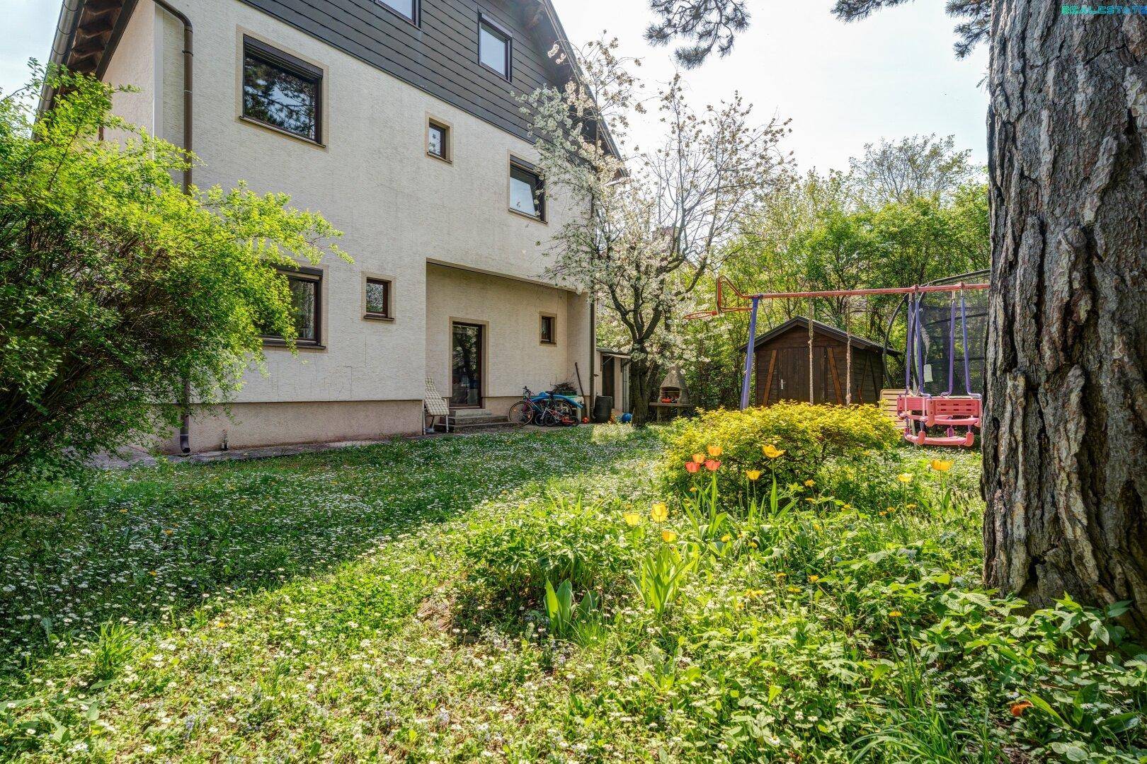 Weitläufiger Garten mit blühenden Pflanzen, einem Schuppen und einem Trampolin im Hintergrund.